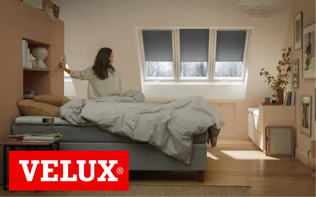 Frau öffnet Verdunkelungsrollos im Schlafzimmer mit Velux-Fenster
